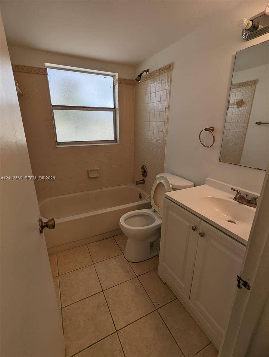 Bathroom featuring tile flooring, a shower-tub combination with tiled surround, a white vanity cabinet, and a single-basin sink