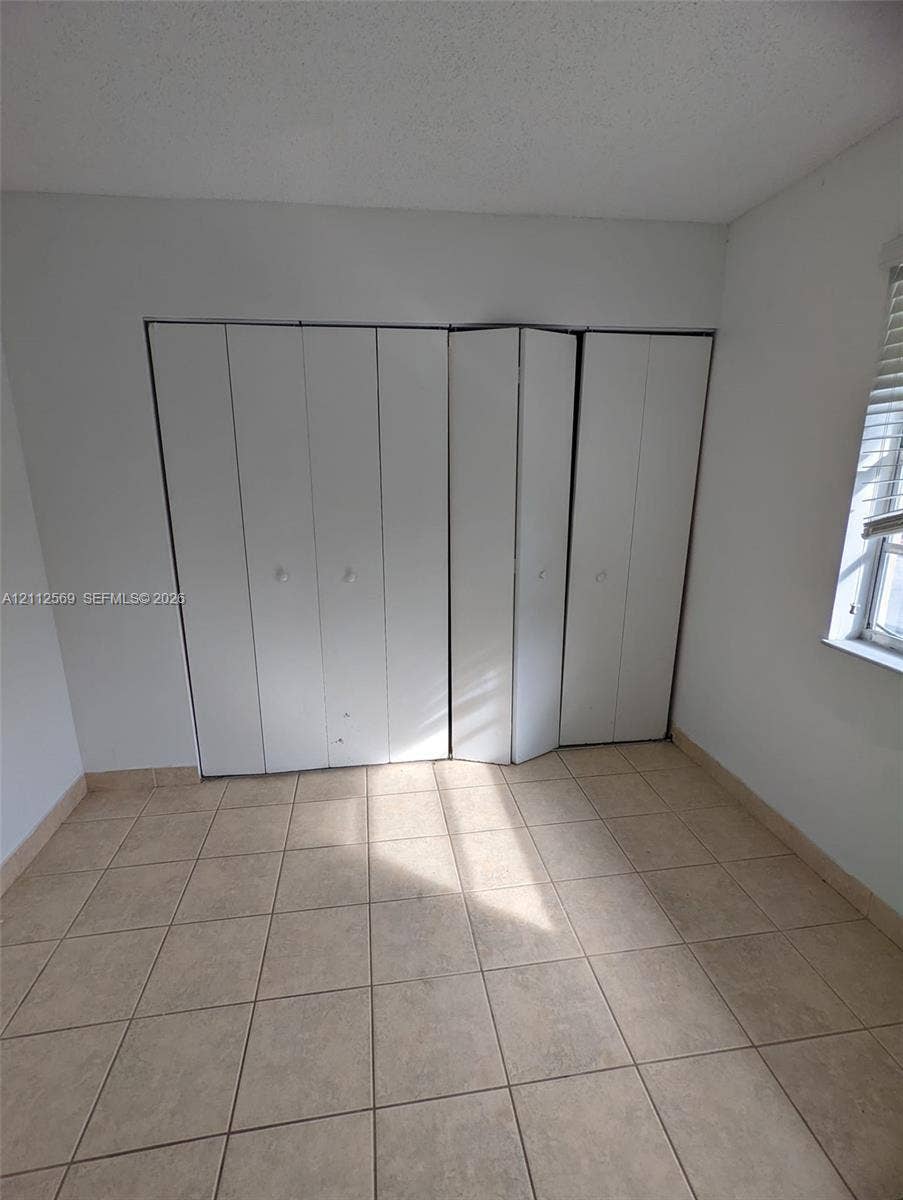 Room featuring neutral ceramic tile flooring, a multi-panel folding closet door, and a single window with horizontal blinds