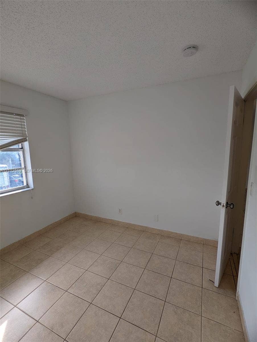 Neutral-toned ceramic tile flooring, single-pane window with horizontal blinds, and a solid-core hinged door