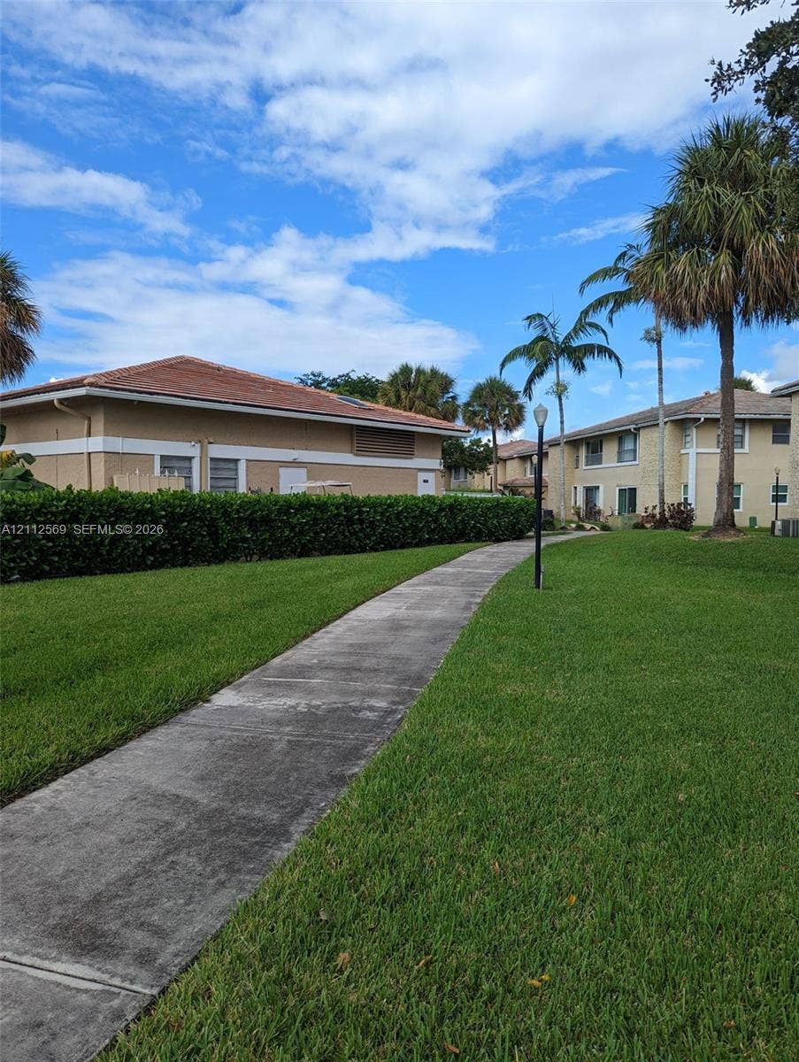Concrete pedestrian path surrounded by landscaped grounds, manicured hedges, mature palm trees, and exterior pole lighting