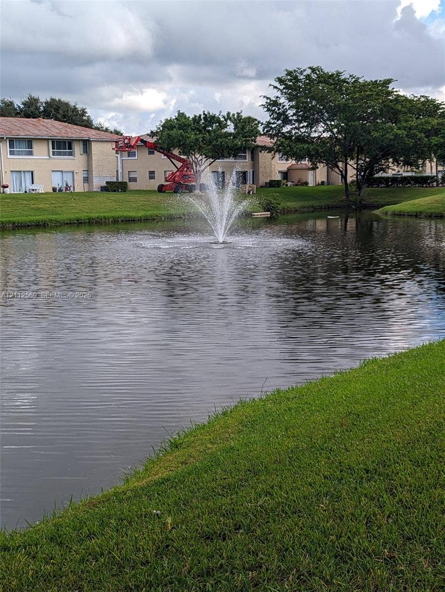 Water feature incorporating a centered fountain set within a natural pond surrounded by manicured turf and mature trees