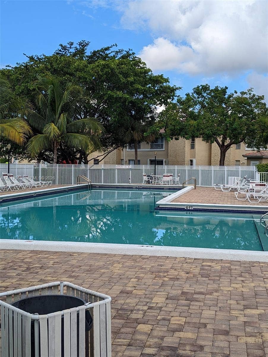 Swimming pool with paver decking and white perimeter fencing, surrounded by mature trees