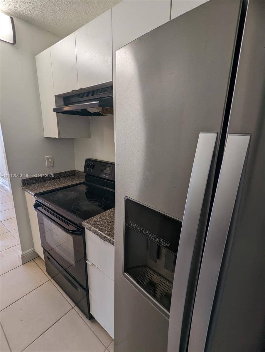 Kitchen featuring flat-panel white cabinetry, speckled stone-finish countertops, black electric range, integrated range hood, and stainless steel side-by-side refrigerator