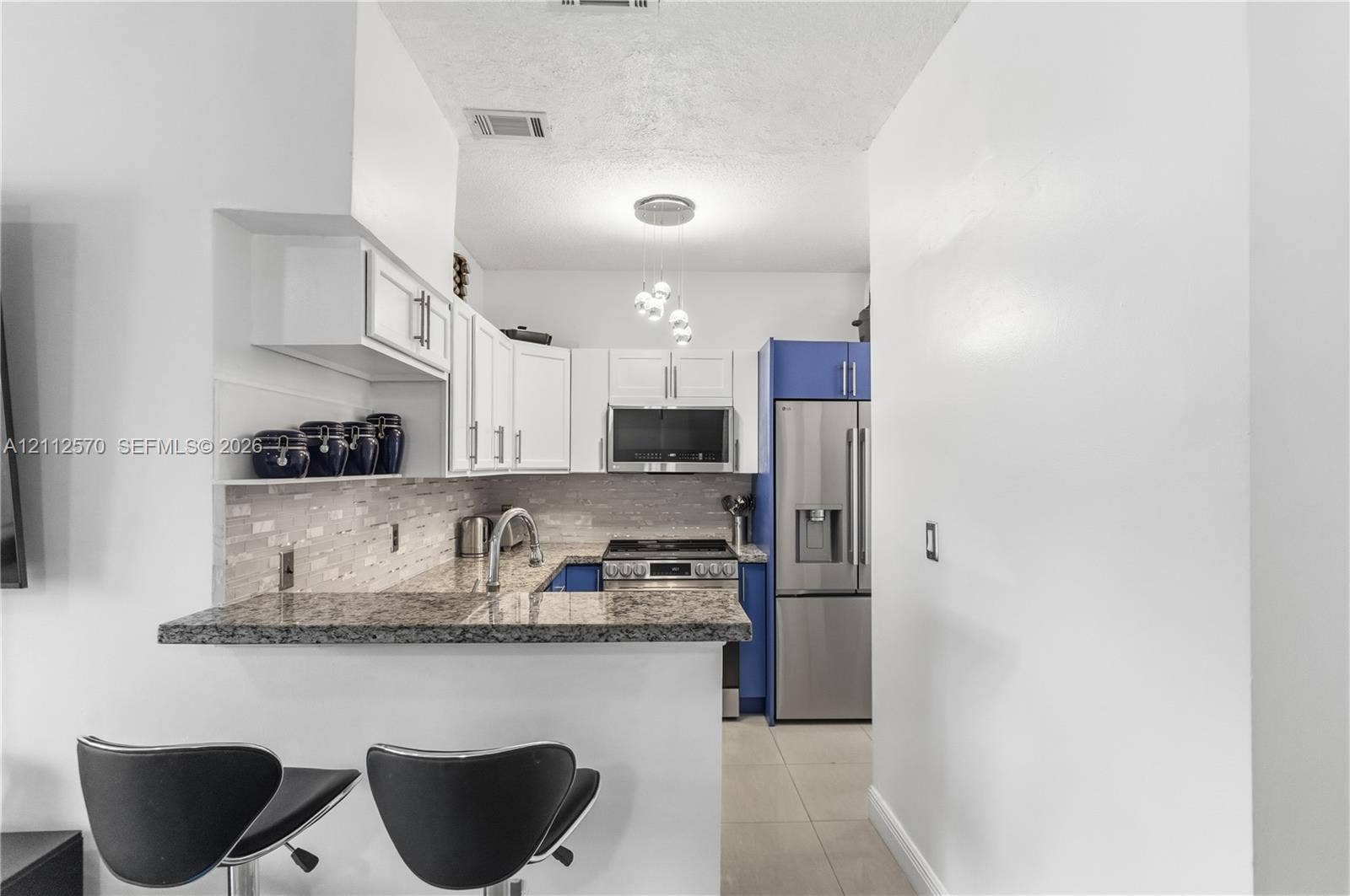Kitchen featuring stone countertops, a multi-tone cabinetry layout with white upper cabinets, stainless steel appliances, and a tiled backsplash