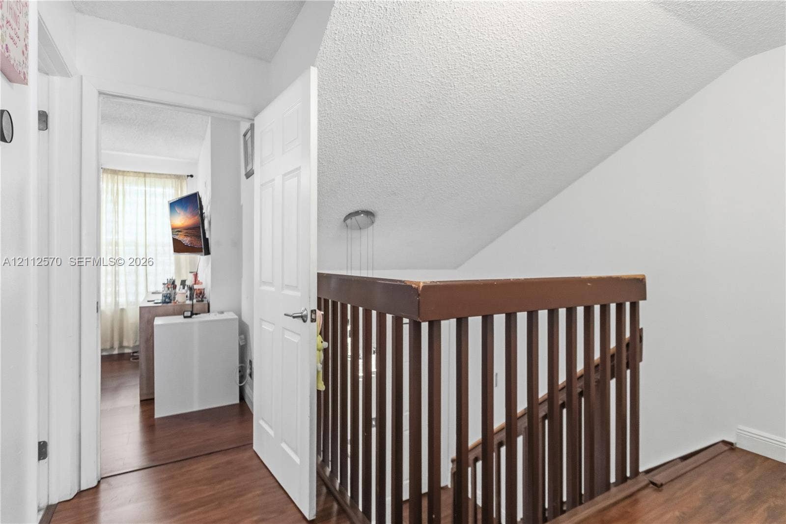 Staircase featuring dark wood-finish railings, wood-finish flooring, and a six-panel door