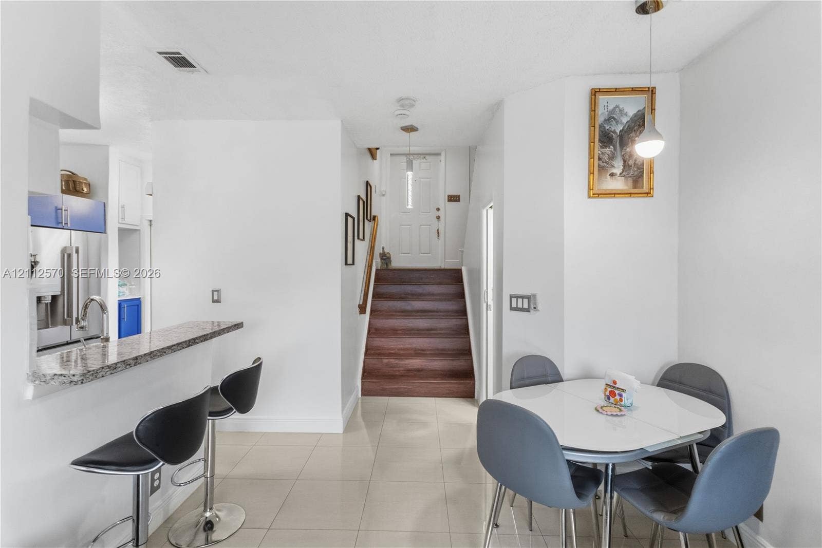 Open-concept kitchen area featuring a stone-topped breakfast bar, tile flooring, and stairs with wood-finish treads leading to an exterior entryway with a glass-paneled door