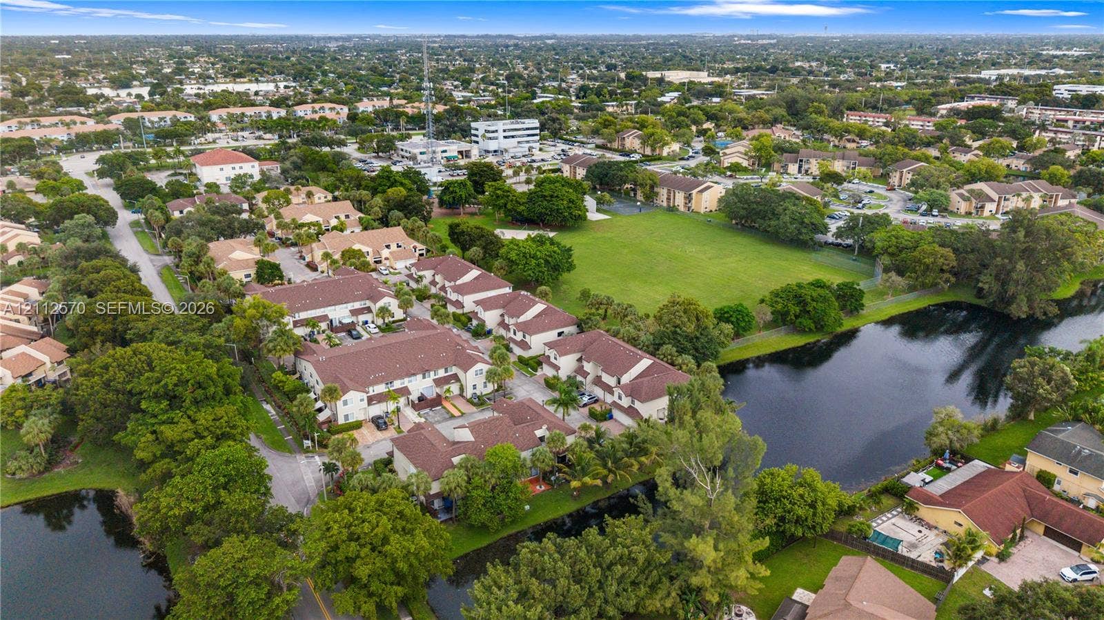 Aerial perspective of a multi-unit residential complex featuring tile roofing, paved parking areas, and mature landscaping situated near a natural pond