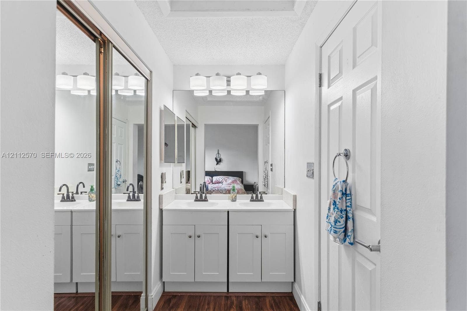 Double vanity featuring white shaker-style cabinetry, solid-surface countertops, dual rectangular drop-in sinks, oil-rubbed bronze fixtures, and a wall-to-wall mirror with overhead light fixture