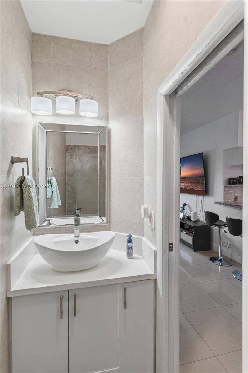 Bathroom featuring a white vanity cabinet, solid-surface countertop, vessel sink with a chrome faucet, tri-light fixture, and framed wall mirror