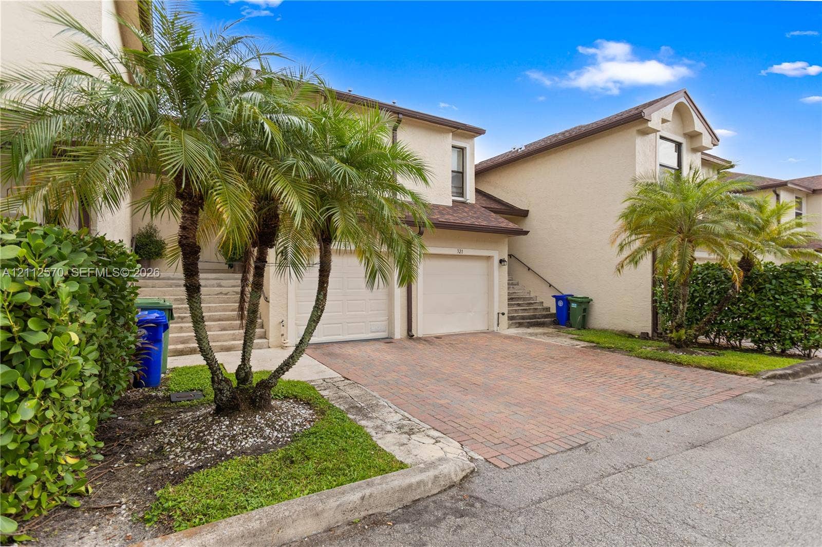 Stucco exterior featuring dual-car garages, brick-paver driveways, external concrete staircases, and established palm tree landscaping