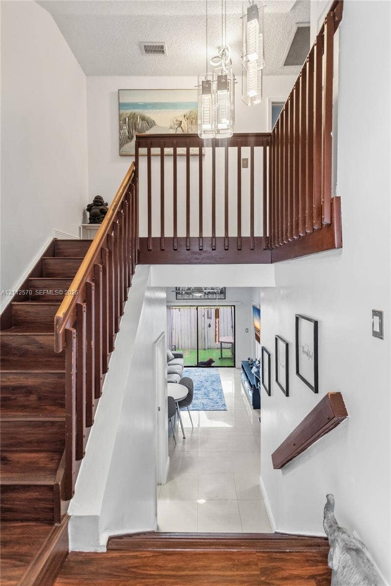 Entryway featuring a wood-finished staircase with matching balustrades, polished tile flooring, and a multi-pendant light fixture