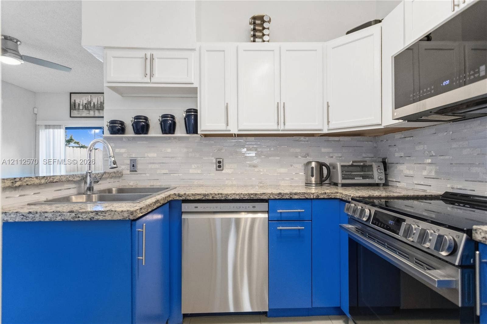 Kitchen featuring two-tone cabinetry, stone-finish countertops, stainless steel appliances, and a mosaic tile backsplash