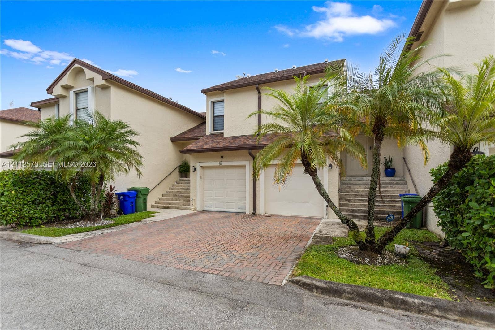 Multi-story exterior featuring a stucco facade, double-car garage, herringbone-pattern brick paver driveway, and stone-tiled staircase