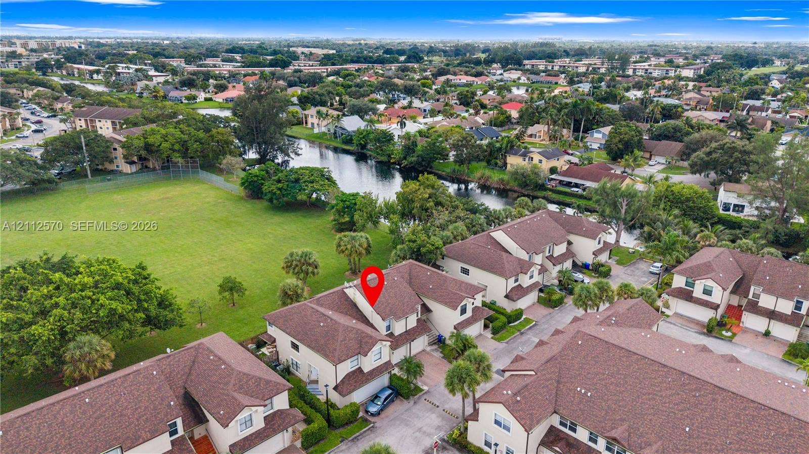 Aerial view of multi-level residential property featuring a pitched shingle roof, attached garage, and surrounding green space