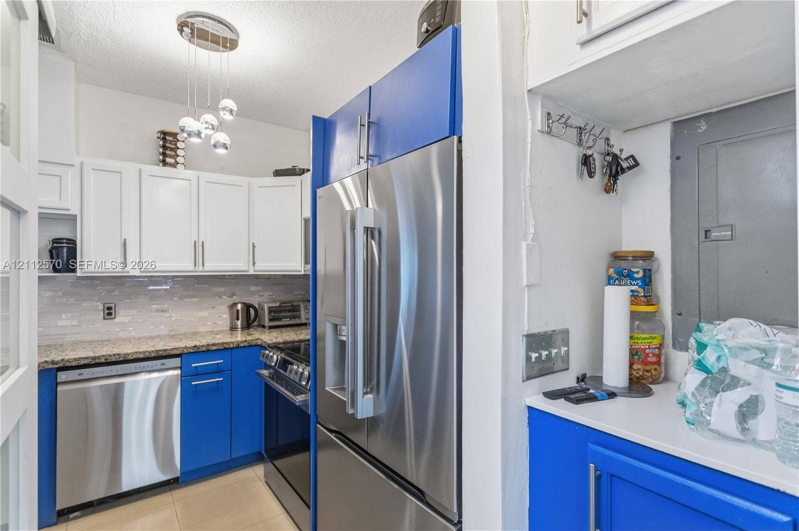 Kitchen featuring high-contrast blue and white cabinetry, stone-finish countertops, stainless steel appliances, a multi-pendant light fixture, and tile flooring