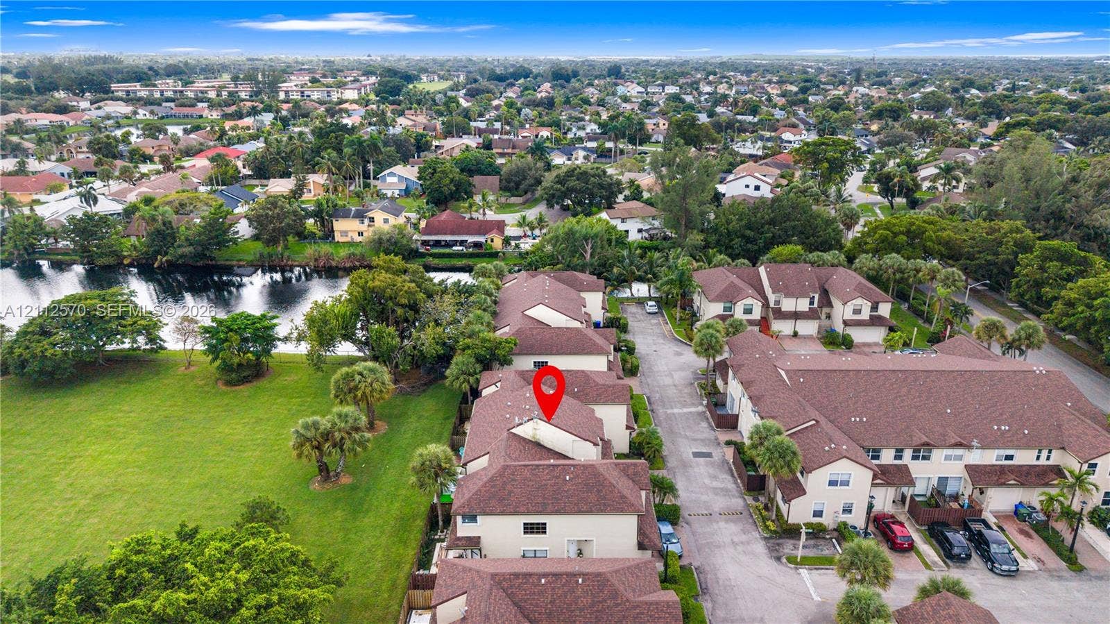 Aerial perspective of a multi-unit property featuring a shingled gable roof, exterior stucco siding, and surrounding landscaped grounds with mature palm trees