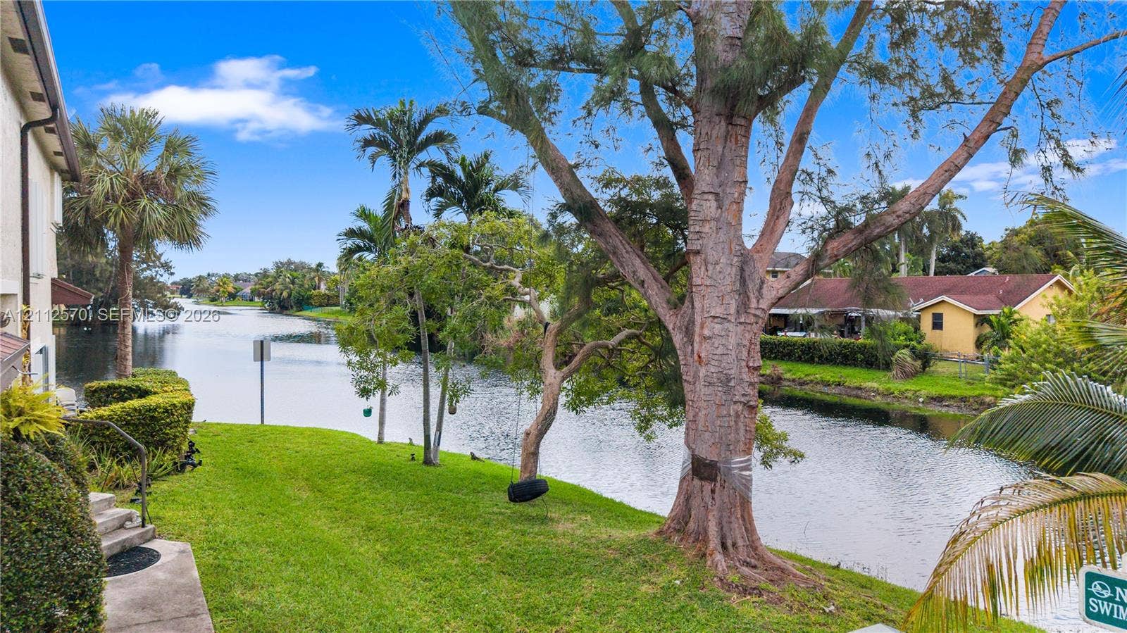 Waterfront backyard featuring a manicured lawn, mature trees, and a concrete path
