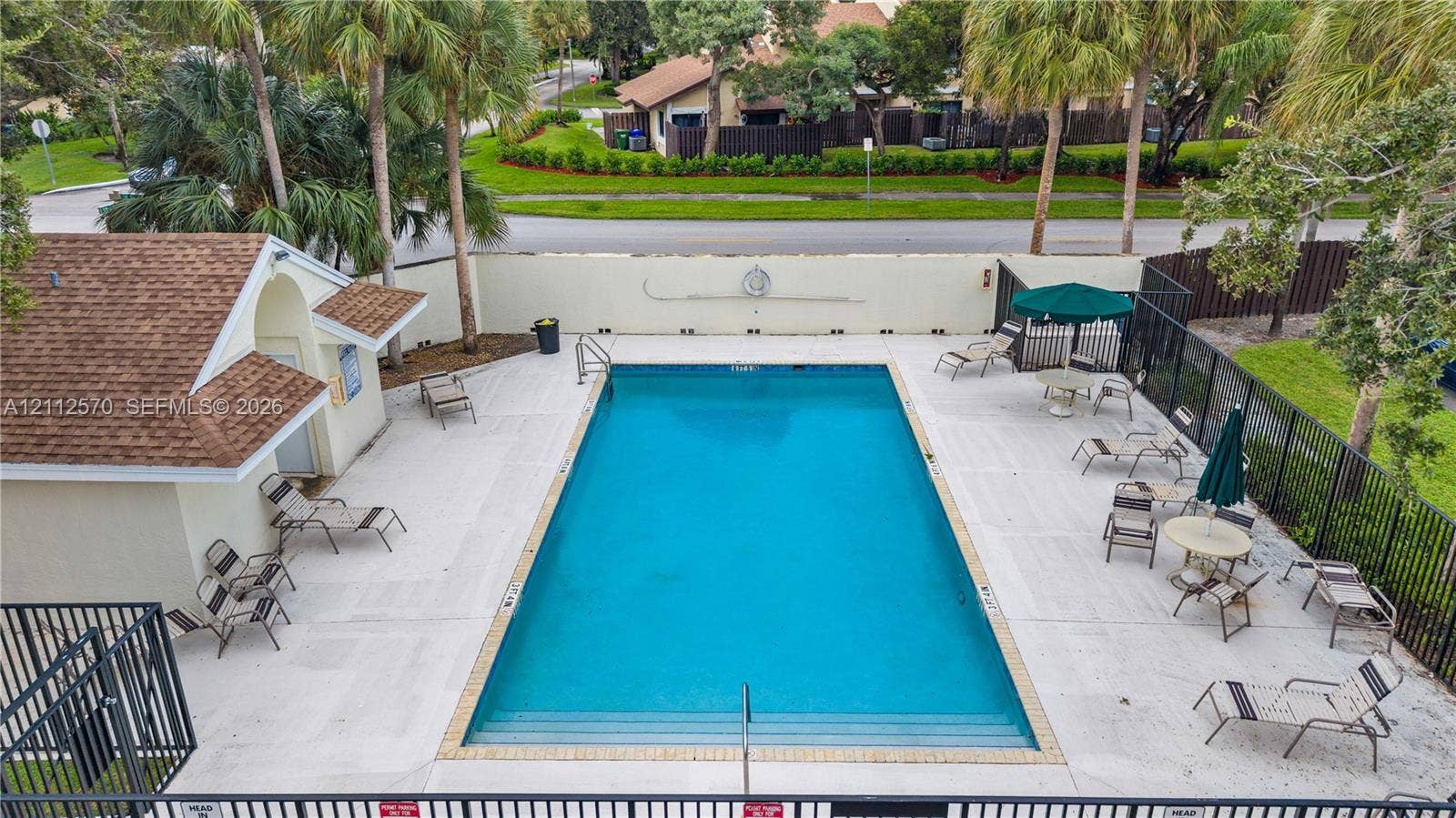 Rectangular swimming pool featuring integrated steps, surrounded by a paved deck, perimeter fencing, and an attached cabana structure