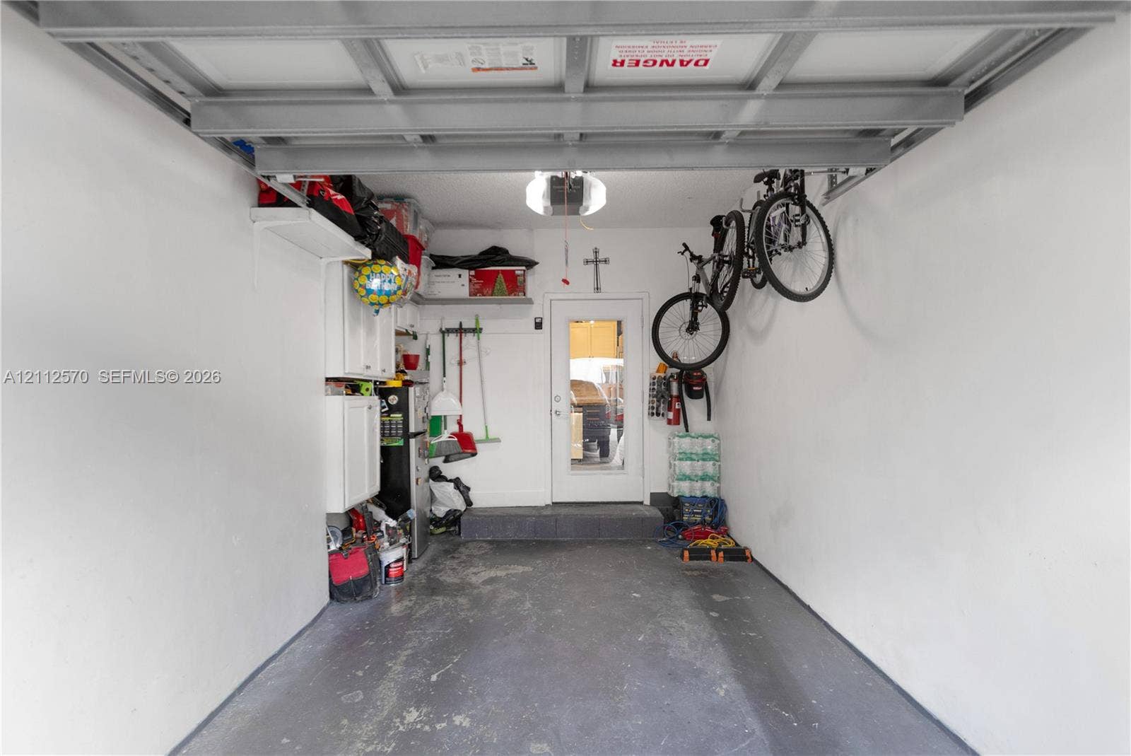 Enclosed garage featuring painted concrete flooring, white cabinetry, overhead lighting, and a single pedestrian entry door with glass paneling