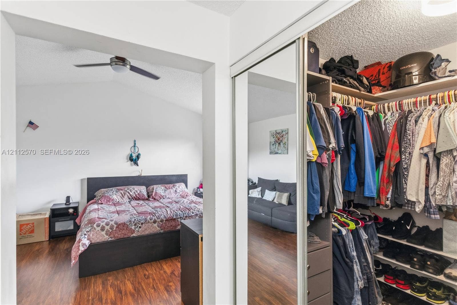 Wood-finish flooring, vaulted ceilings, ceiling fan, and walk-in closet featuring mirrored sliding doors and built-in shelving