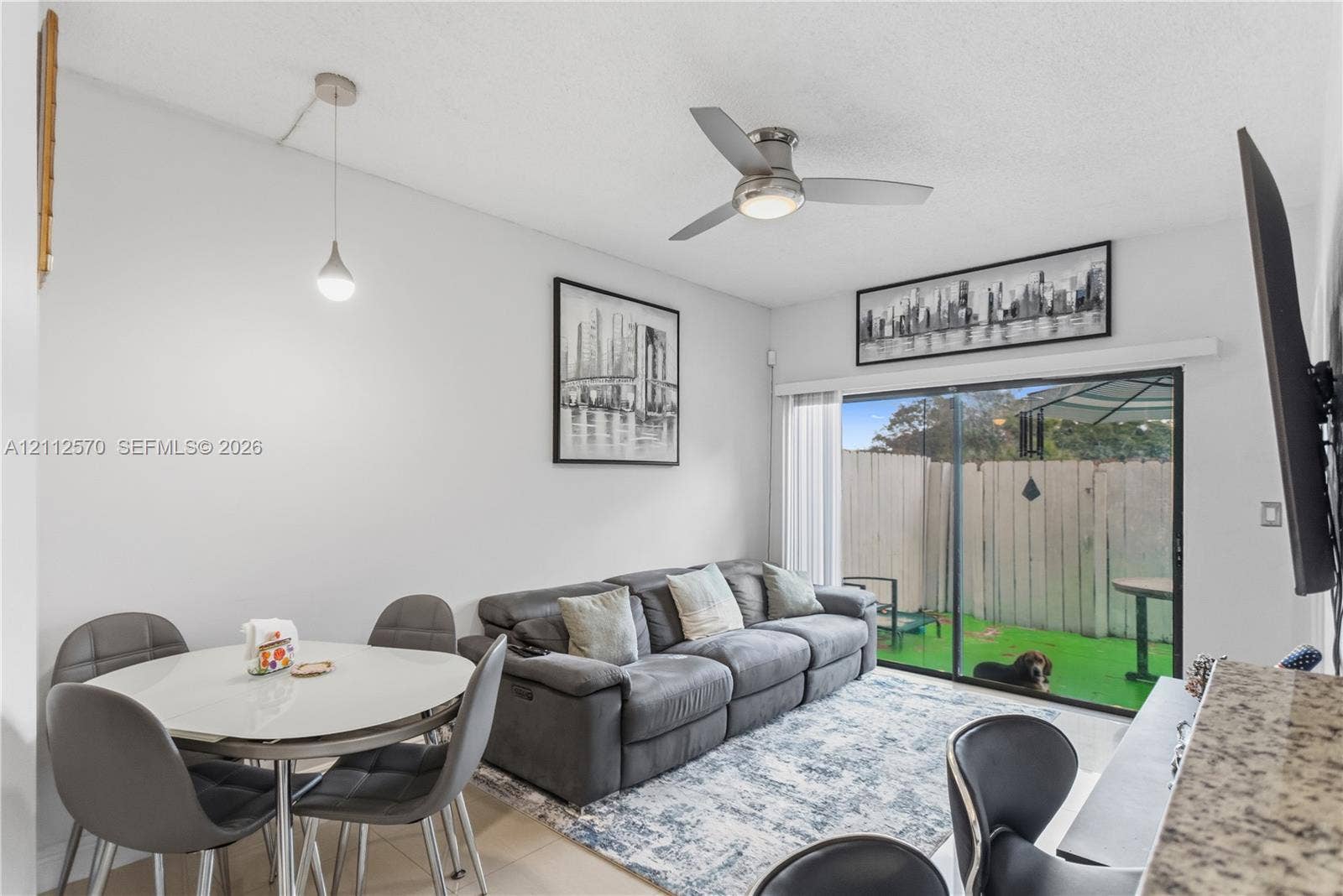 Living space featuring a ceiling fan, a pendant light fixture, and a sliding glass door providing external access to a fenced patio area