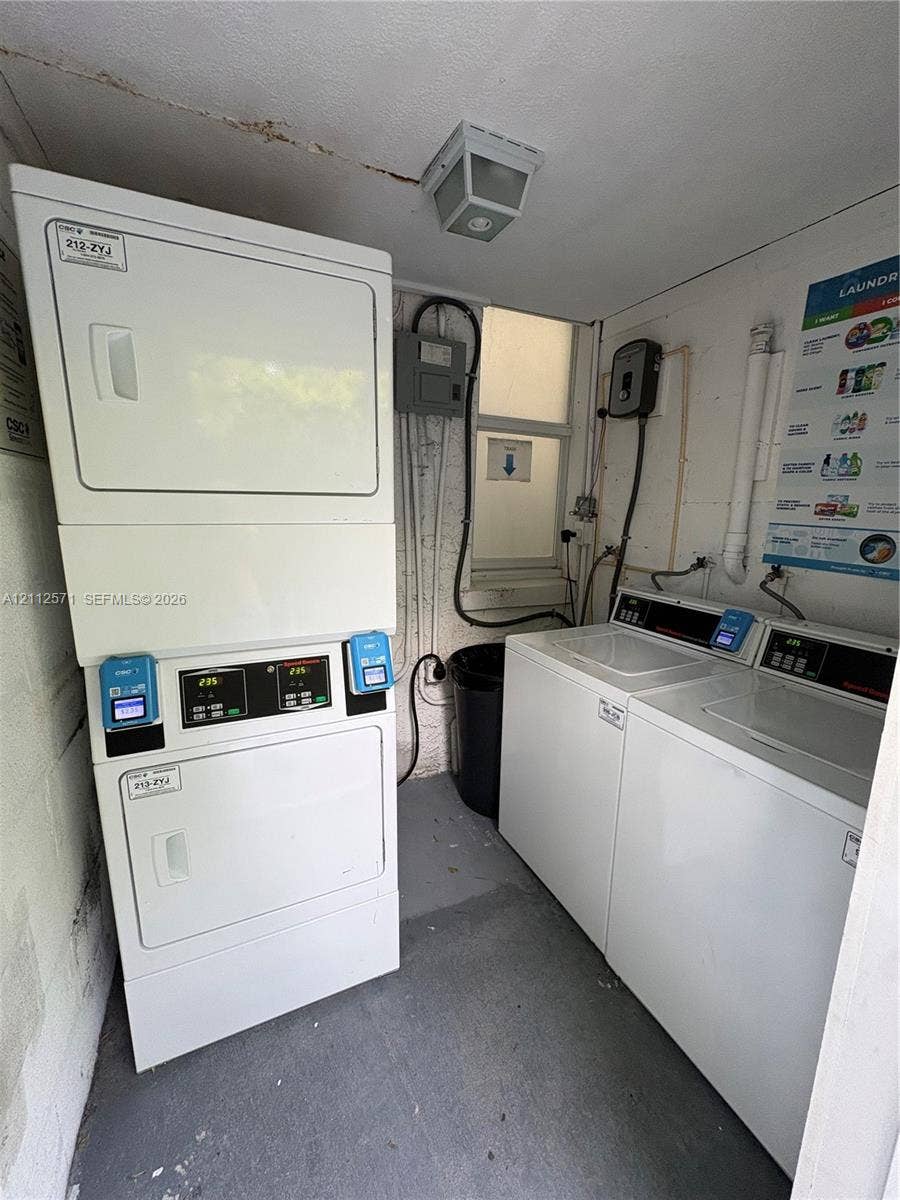 Laundry area featuring a stacked washer-dryer unit and side-by-side laundry machines, illuminated by a ceiling-mounted light fixture and natural light from a window