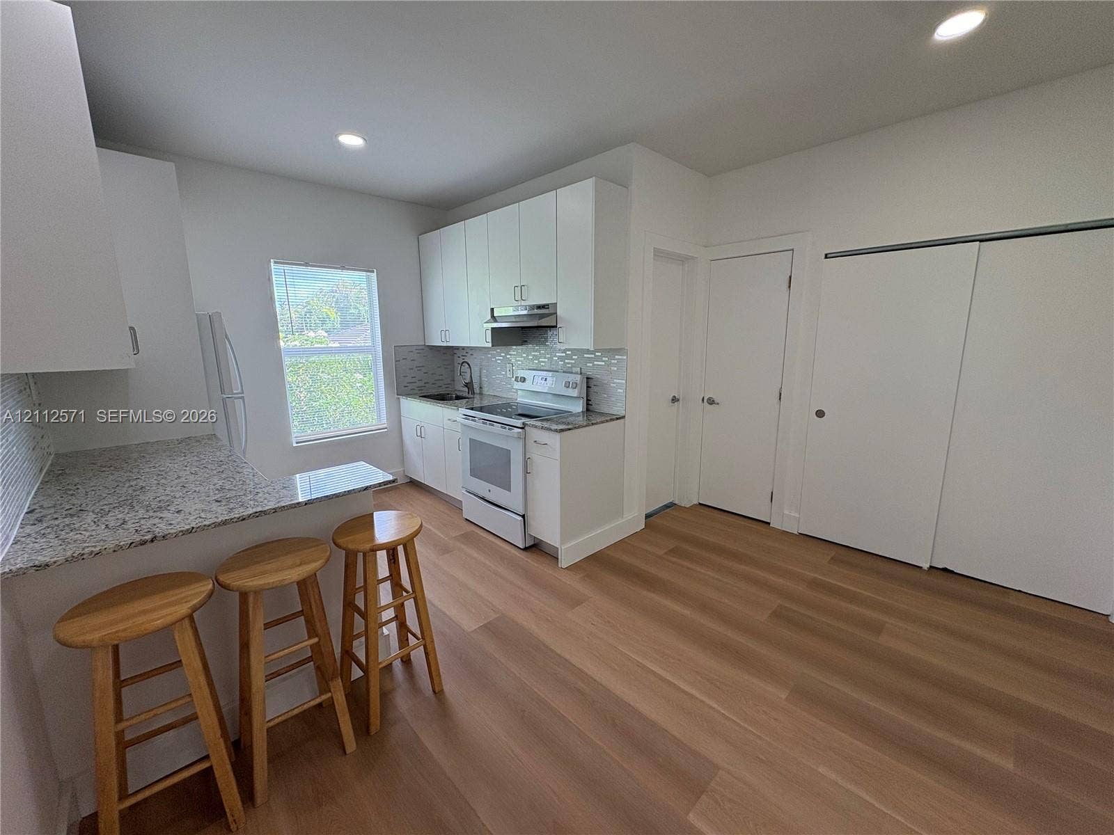 Kitchen featuring white cabinetry, stone-surface countertops, tile backsplash, recessed lighting, and wood-finish flooring
