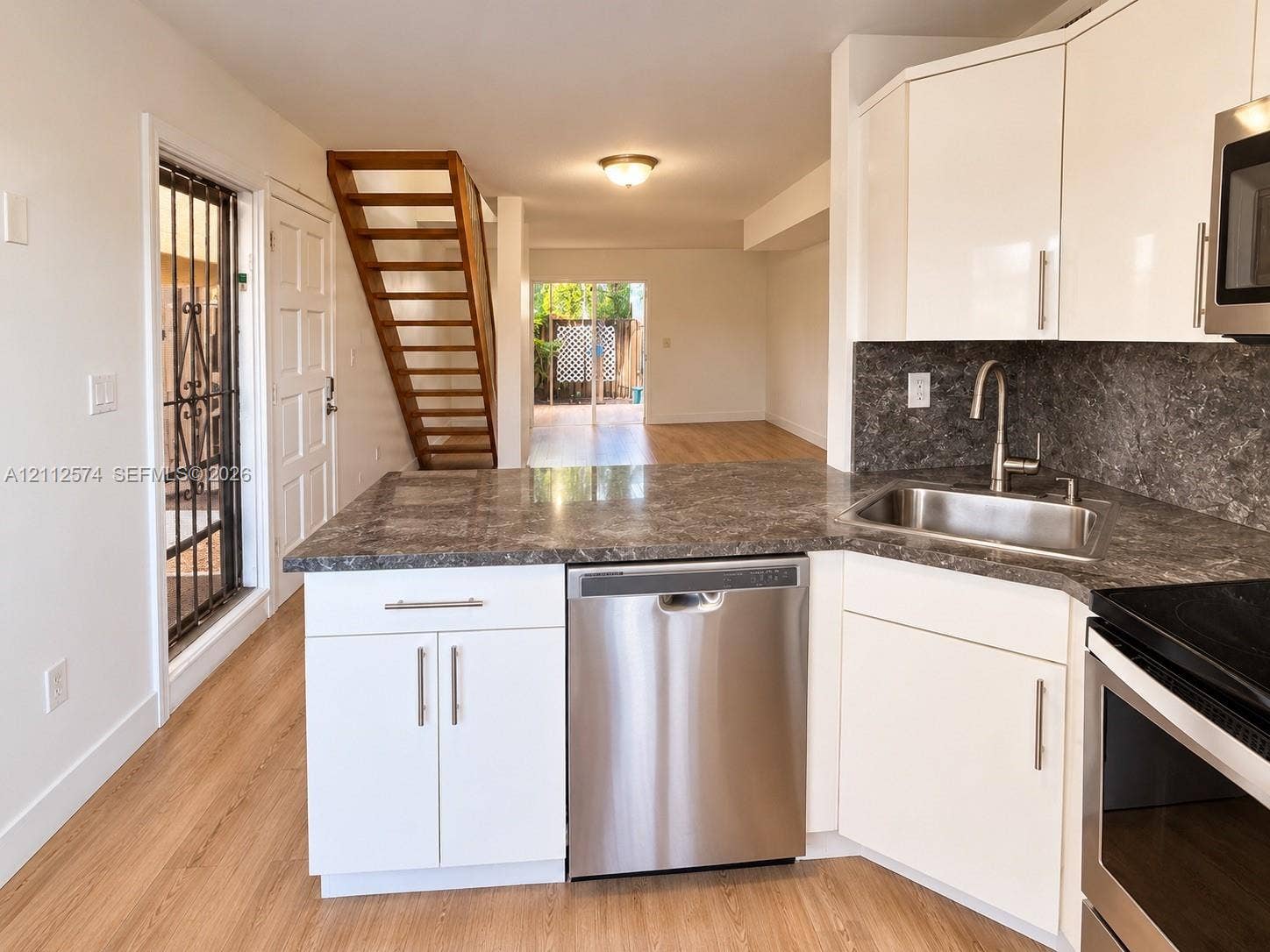 Kitchen featuring white cabinetry, stone-finish countertops, stainless steel appliances, wood-finish flooring, and an open-tread staircase