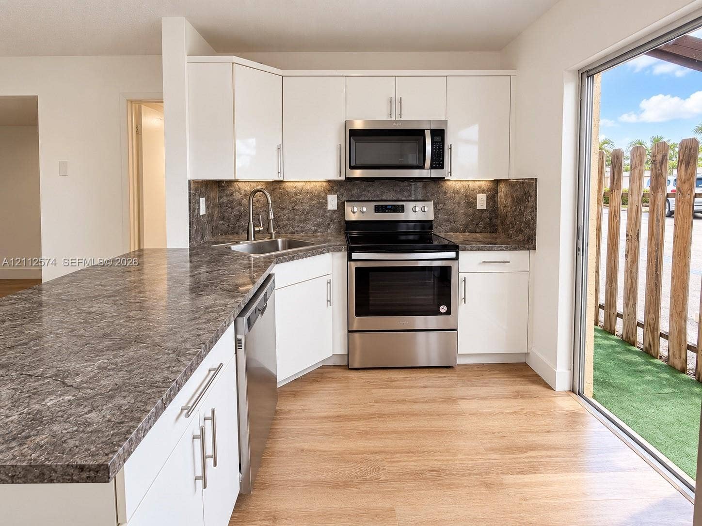 Kitchen featuring white flat-panel cabinetry, stone-finish countertops, stainless steel appliances, under-cabinet lighting, and wood-finish flooring
