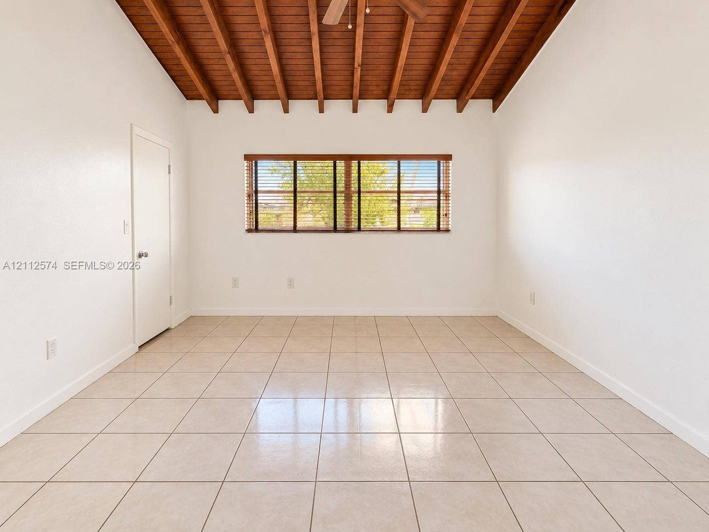 Exposed wood-beam vaulted ceiling featuring an integrated ceiling fan, large-format tile flooring, and horizontal window blinds