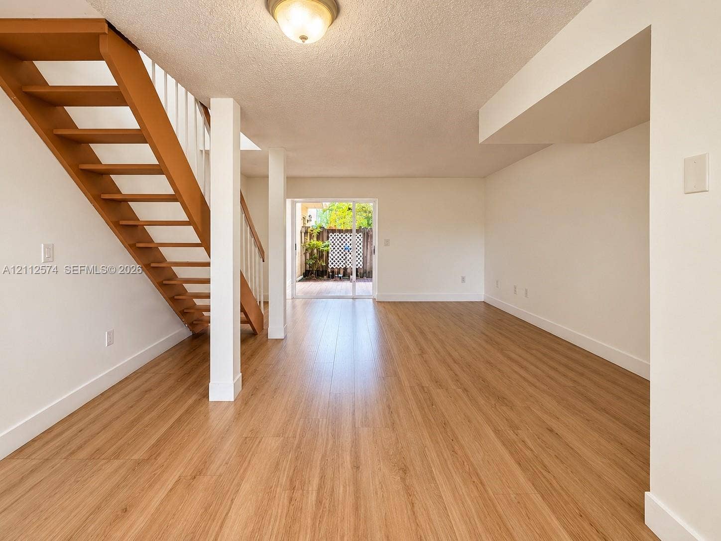 Open-concept space featuring wood-finish flooring, a floating wooden staircase with vertical white balusters, structural support columns, and sliding glass doors