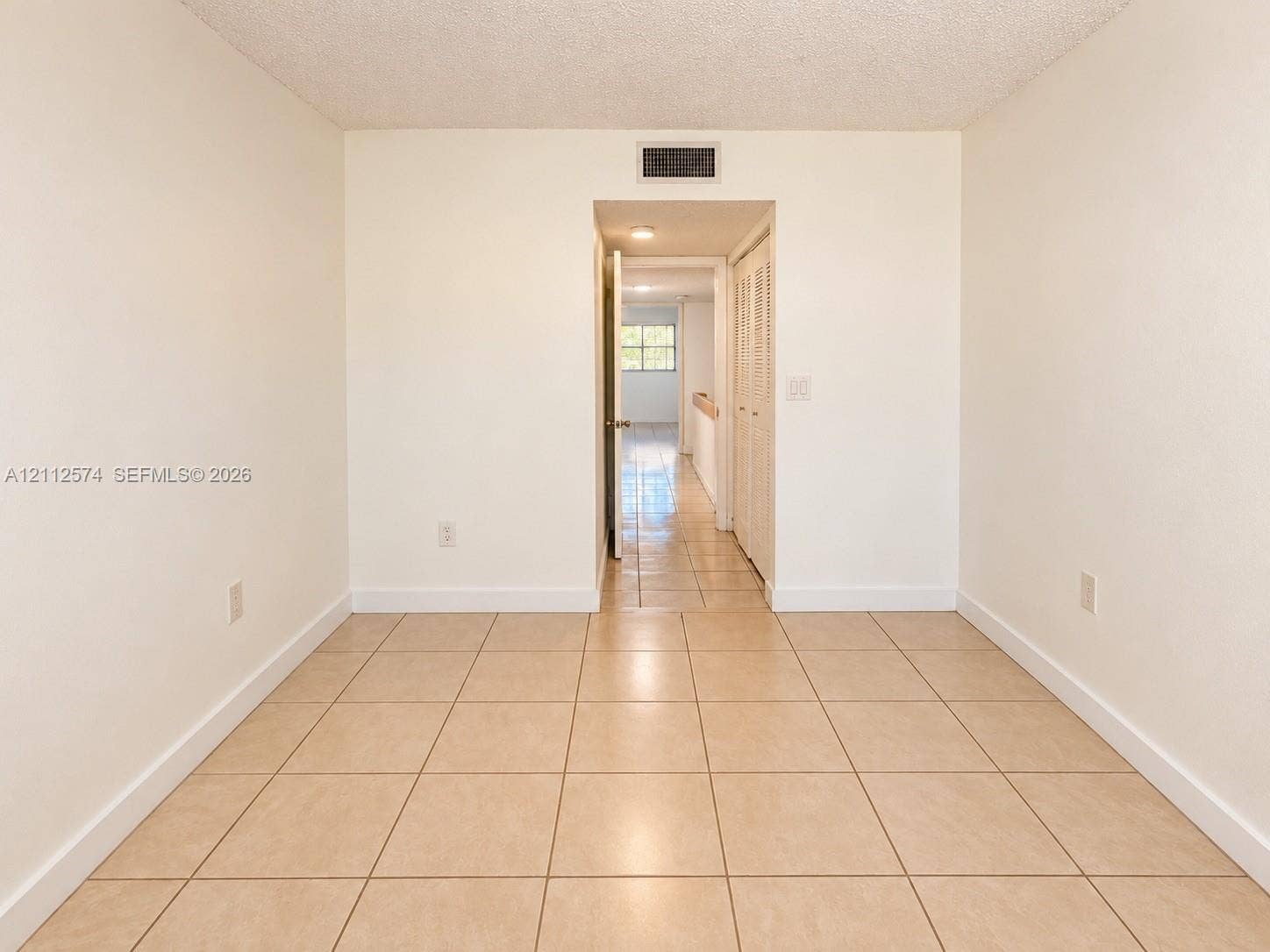 Neutral-toned room featuring uniform ceramic tile flooring, a solid-core interior door, and bi-fold closet doors