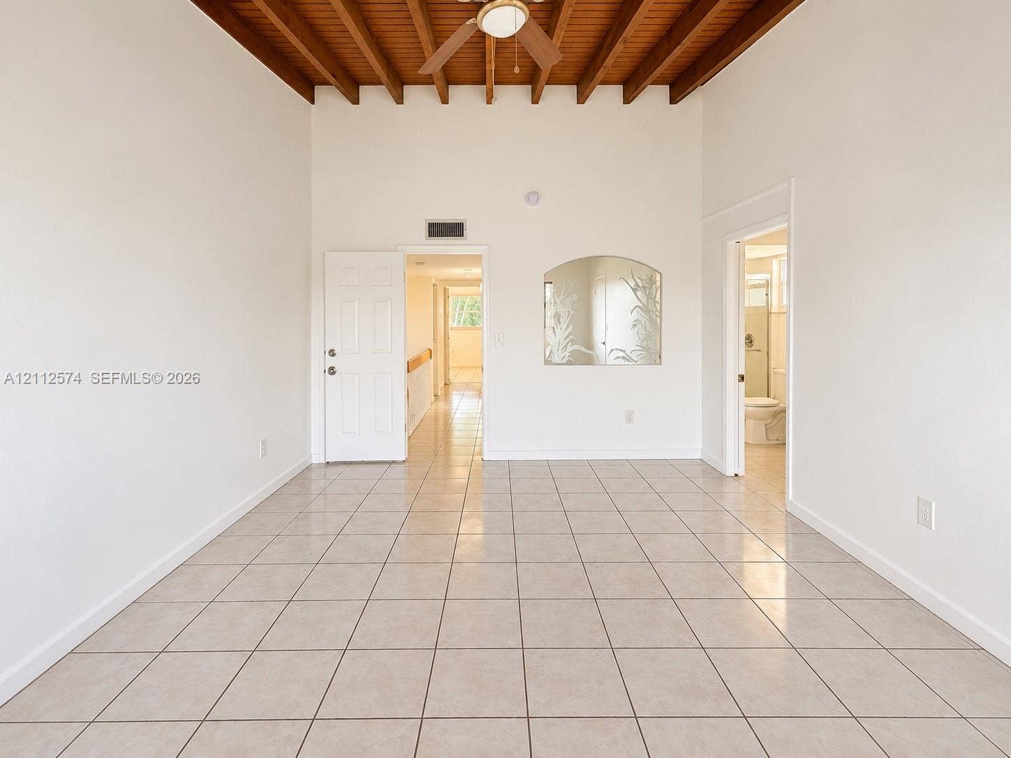 Exposed wood-beam ceiling, light-toned tile flooring, and integrated ceiling fan