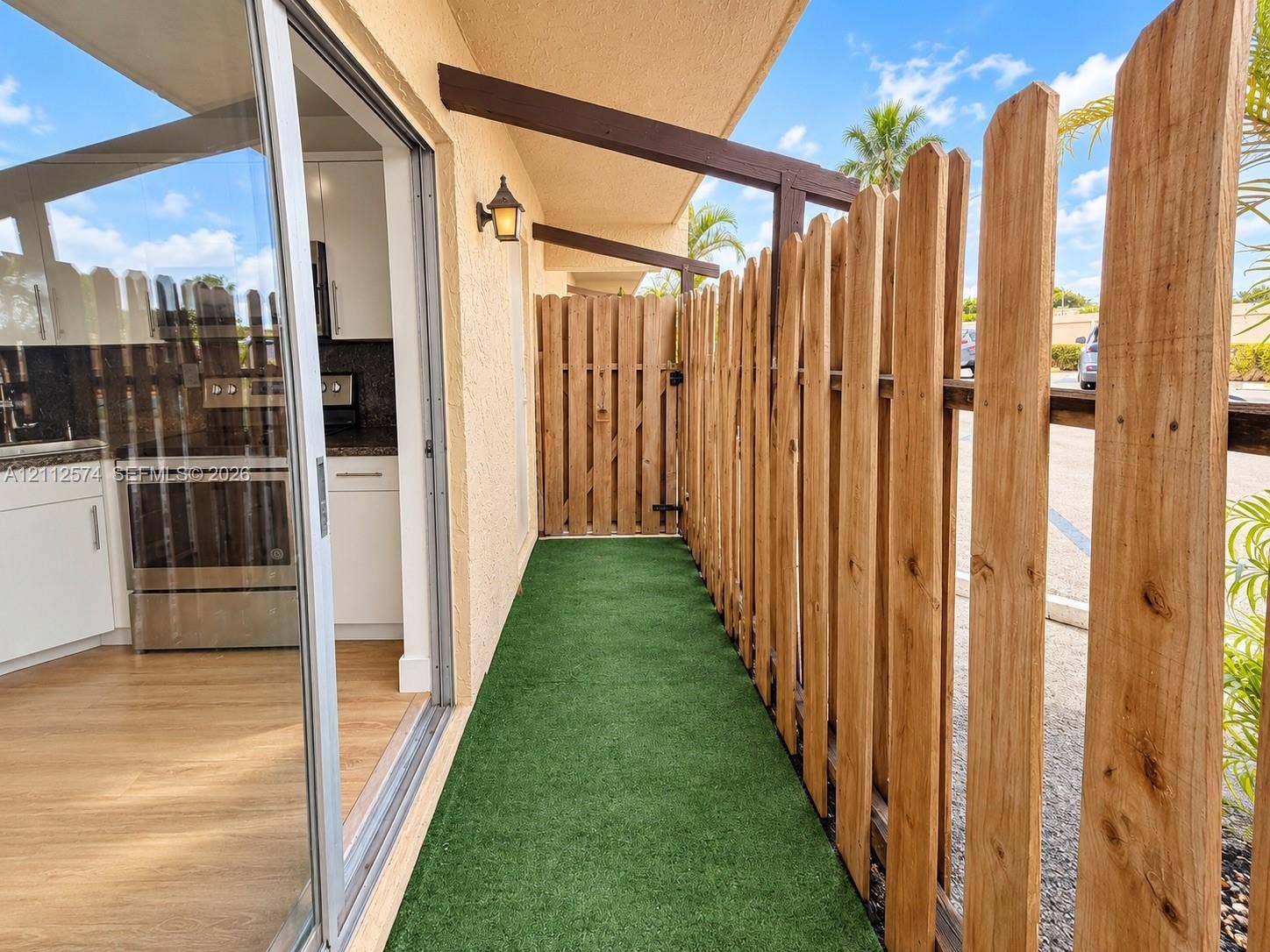 Private outdoor space featuring synthetic turf, vertical wood fencing with a gate, and exterior wall-mounted lighting