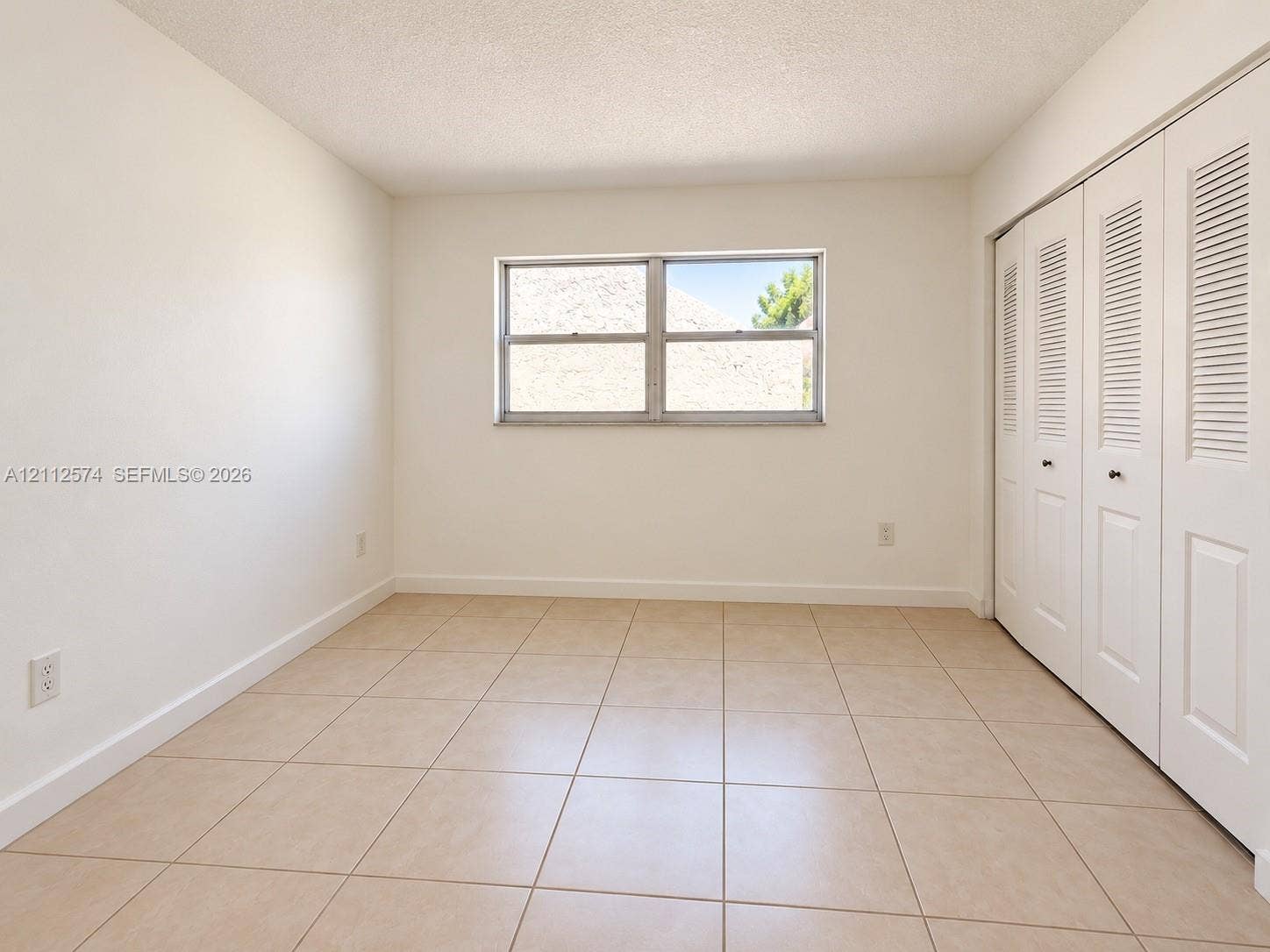 Neutral tile flooring, sliding louvered closet doors, and a double-pane horizontal window