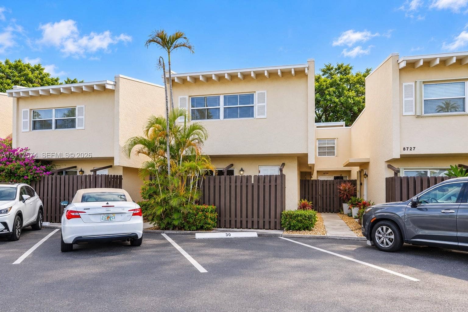 Stucco exterior featuring exposed rafter tails, private fenced courtyards, designated parking, and mature palm landscaping