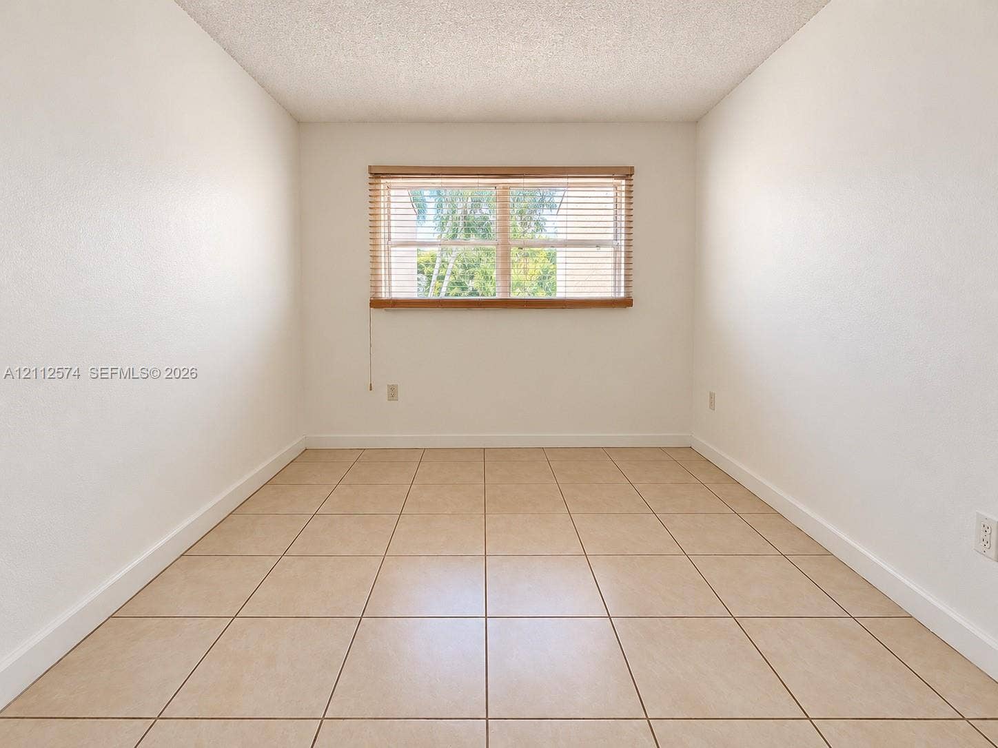 Neutral-toned tile flooring, textured ceiling, and a large central window with horizontal slat blinds
