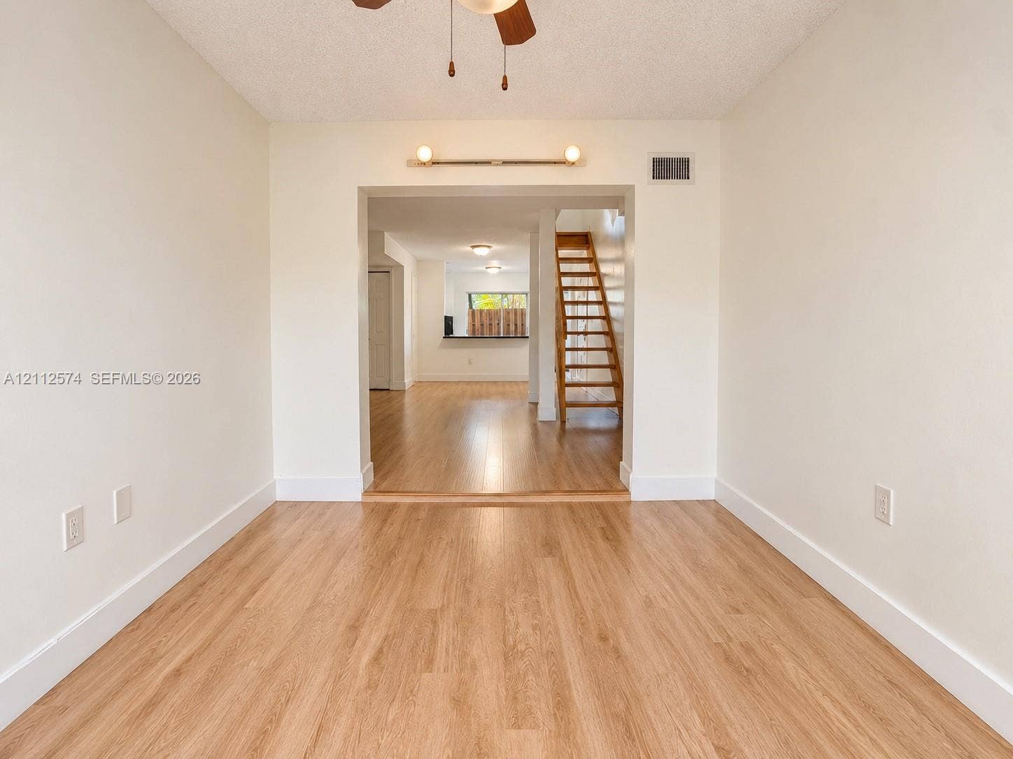 Wood-finish flooring, neutral wall tones, ceiling fan with integrated lighting, wall-mounted fixture, and wooden staircase