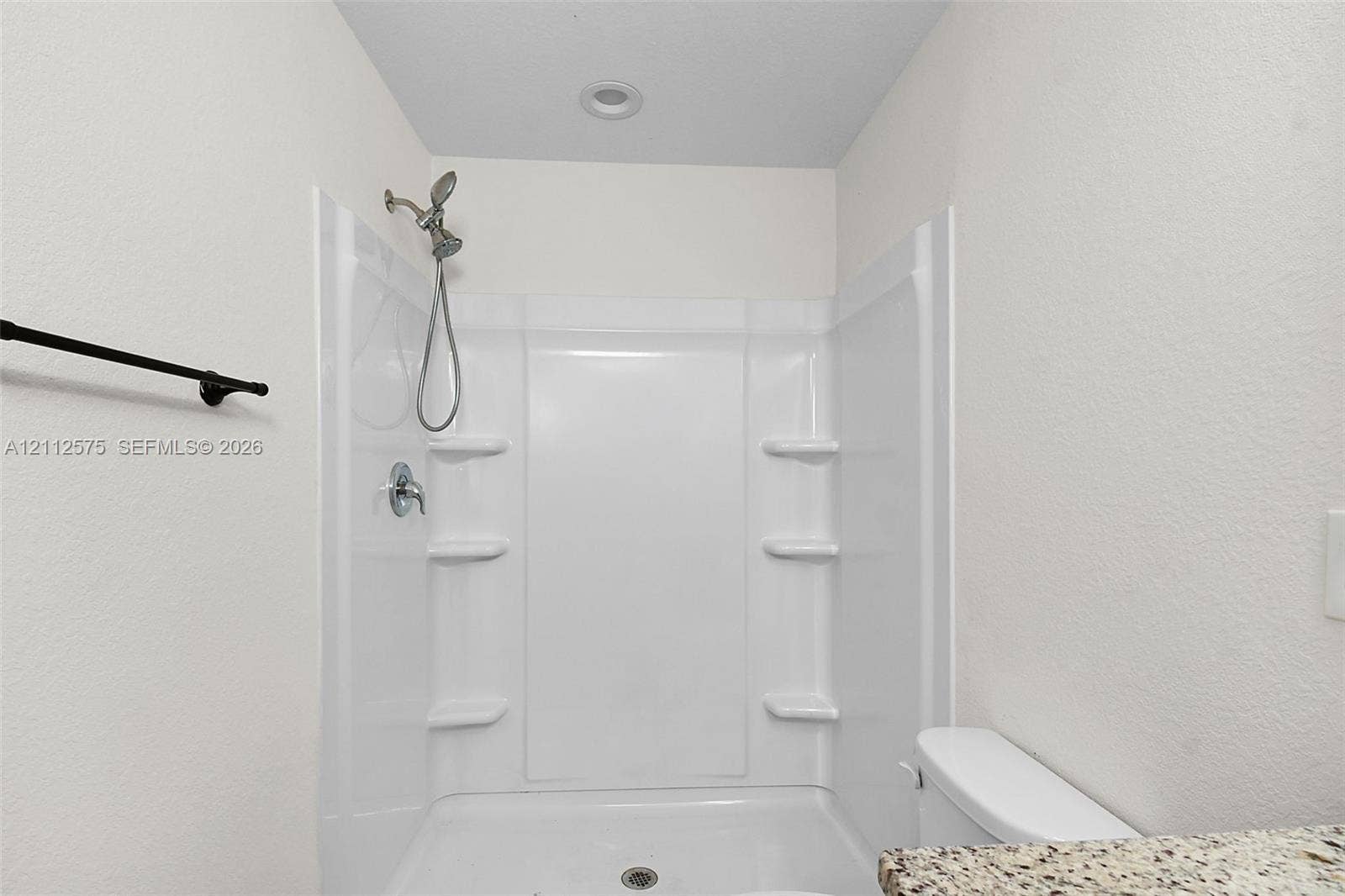 9041 E Broad, Labelle, FL 33935 Walk-in shower enclosure with integrated shelving, handheld showerhead, recessed ceiling lighting, and a stone-finish countertop