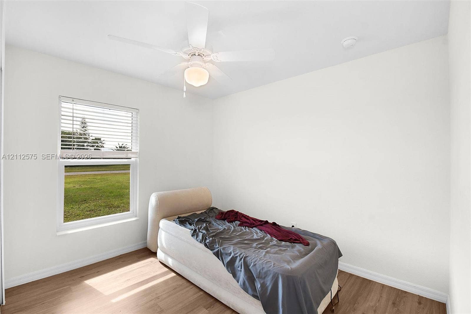 9041 E Broad, Labelle, FL 33935 Room featuring wood-finish flooring, a white ceiling fan with integrated lighting, and a single-pane window with horizontal blinds