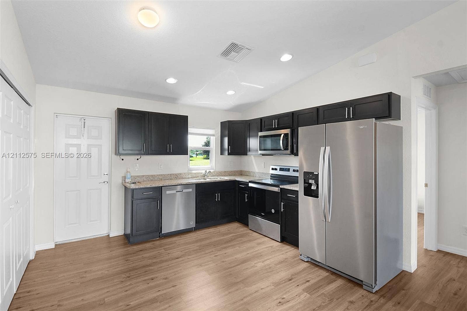 9041 E Broad, Labelle, FL 33935 Kitchen featuring dark cabinetry, stone-surface countertops, wood-finish flooring, and stainless steel appliances including a side-by-side refrigerator, microwave, and dishwasher
