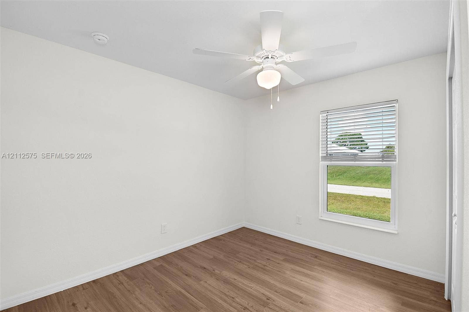 9041 E Broad, Labelle, FL 33935 Interior room featuring wood-finish flooring, white walls, a ceiling fan with integrated lighting, and a single-hung window with blinds