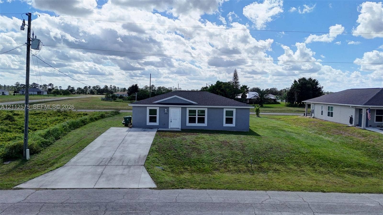 9041 E Broad, Labelle, FL 33935 Single-story residence featuring a gray exterior, gabled roofline, crisp white trim, and a concrete driveway