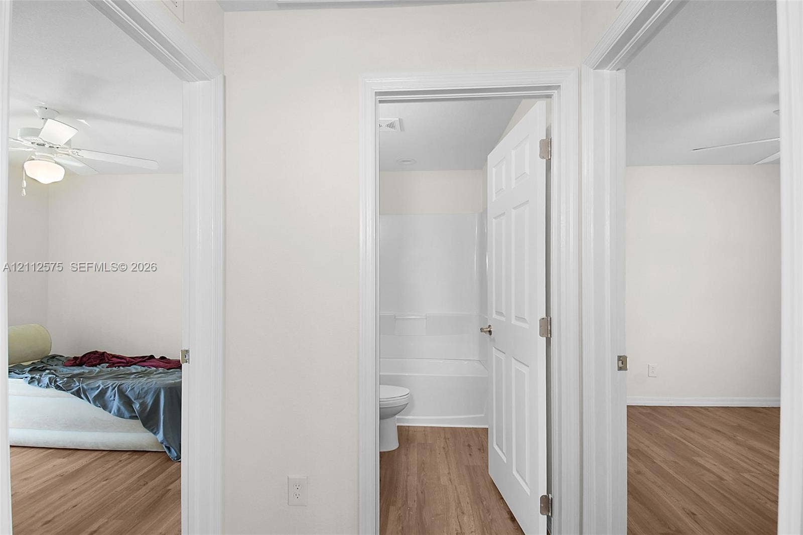9041 E Broad, Labelle, FL 33935 Interior hallway featuring wood-finish flooring, white six-panel doors, and a bathroom equipped with a white tub-shower surround