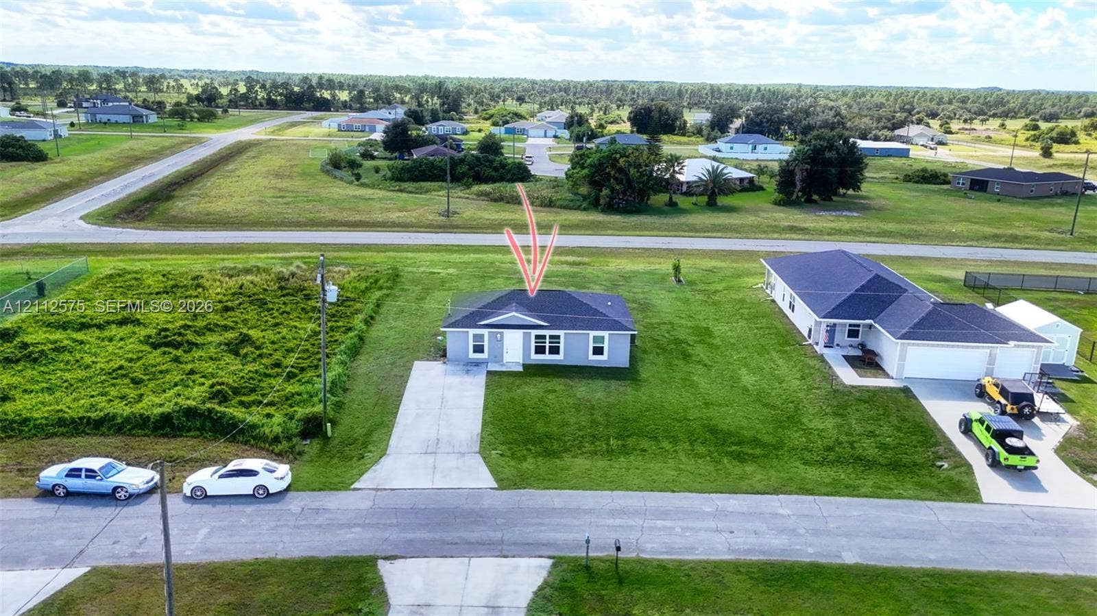 9041 E Broad, Labelle, FL 33935 Single-story residence featuring a hipped roof, light-toned exterior siding, and an expansive lot with a paved driveway