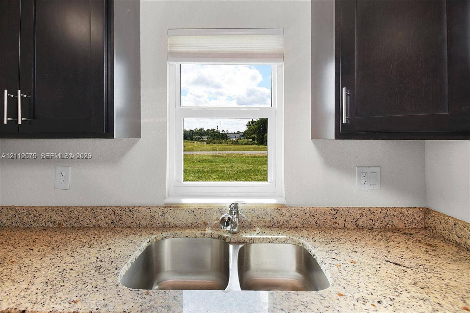 9041 E Broad, Labelle, FL 33935 Deep-toned cabinetry featuring vertical pulls, speckled stone countertops, dual-basin stainless steel sink, and a centralized window with integrated shade