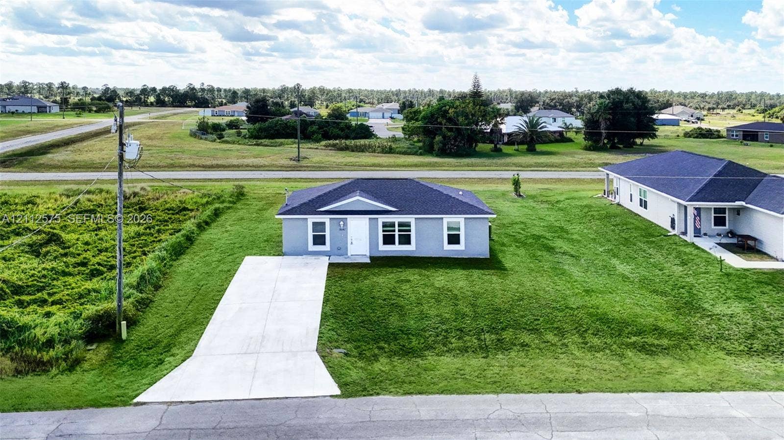 9041 E Broad, Labelle, FL 33935 Single-story residence featuring a gray exterior, dark shingle roof, white window trim, and a concrete driveway