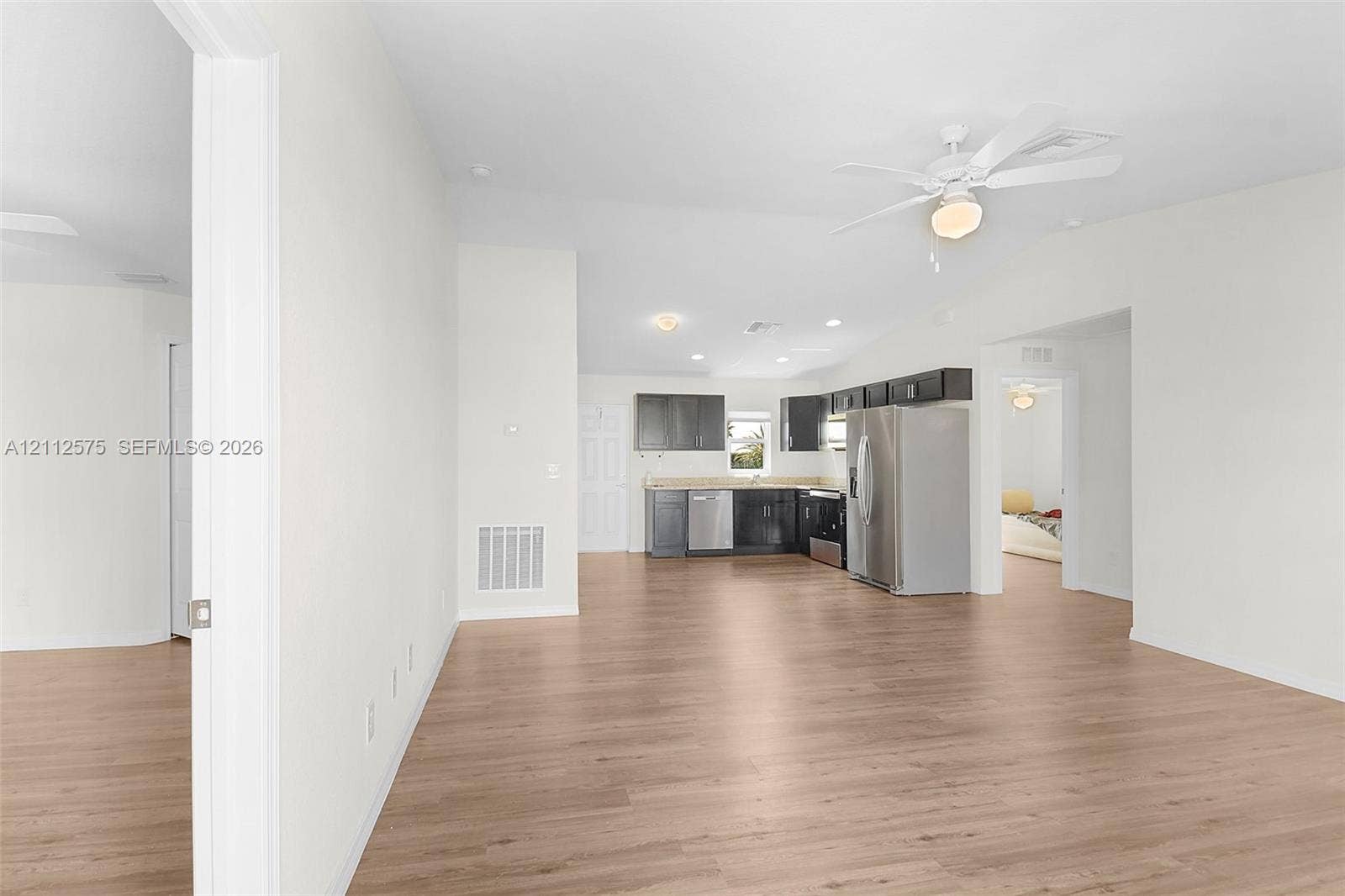 9041 E Broad, Labelle, FL 33935 Open-concept interior featuring light wood-finish flooring, vaulted ceilings with a mounted paddle fan, and a kitchen equipped with dark-toned cabinetry, light-colored countertops, and stainless steel appliances