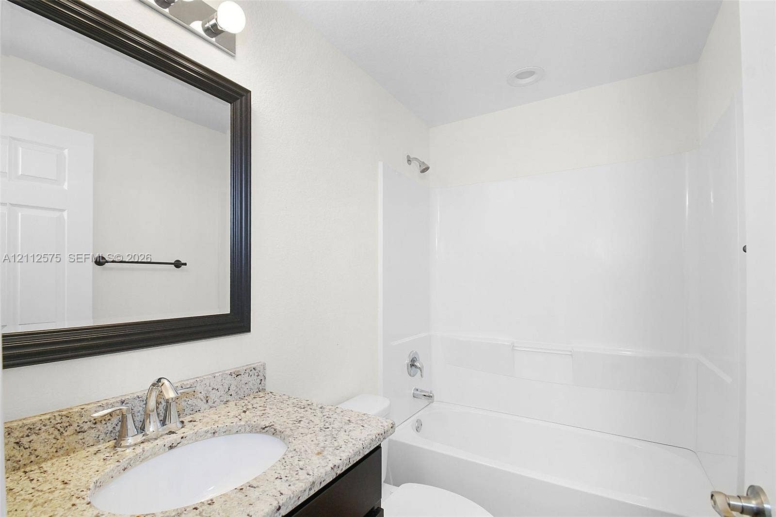 9041 E Broad, Labelle, FL 33935 Bathroom featuring a stone-look countertop, undermount sink, dark-framed mirror, and a combination tub and shower surround