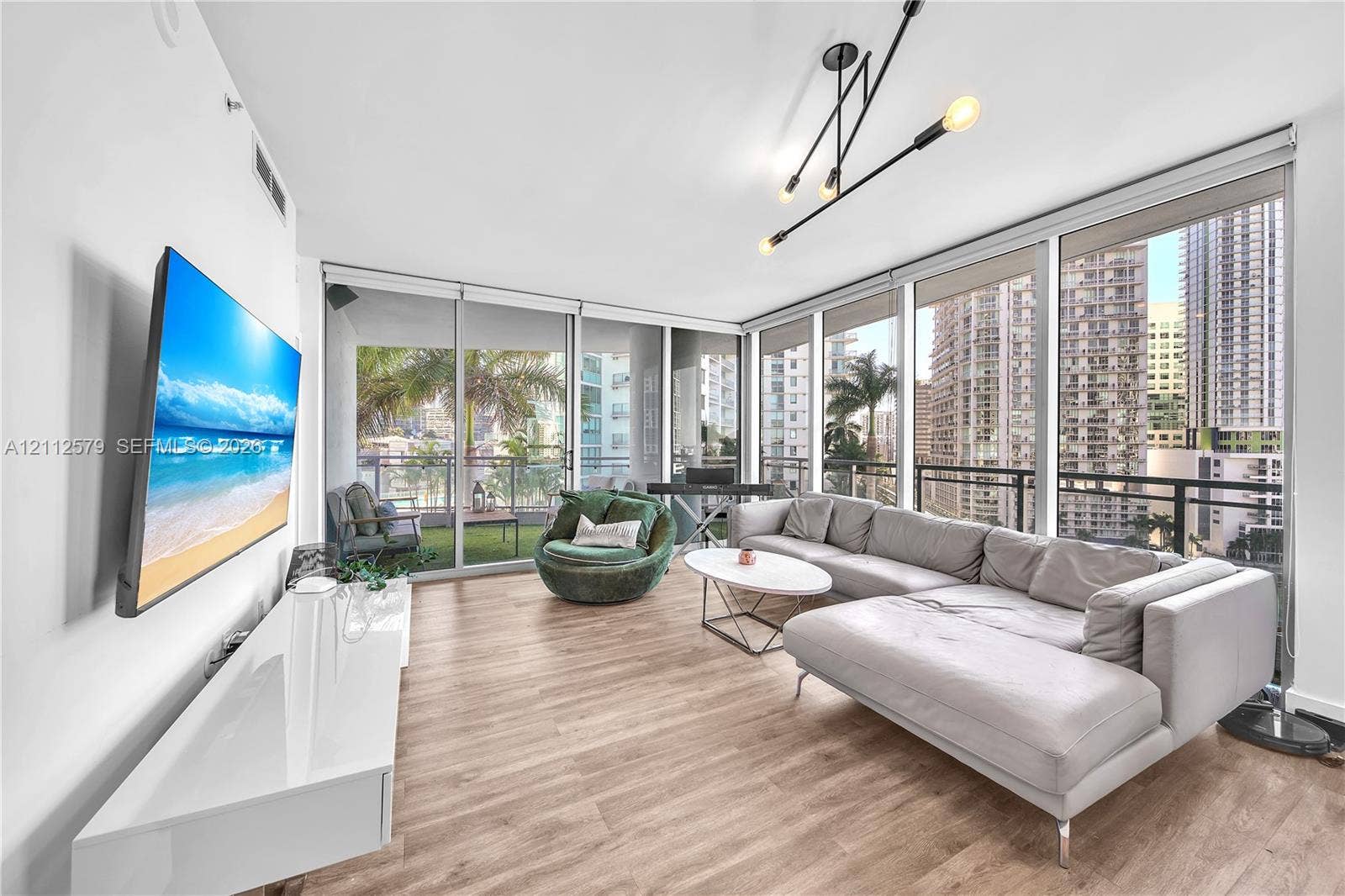Floor-to-ceiling windows, wood-finish flooring, linear multi-arm light fixture, and an attached balcony with metal railing